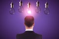 Back view of young european businessman looking at abstract glowing row of light bulbs on purple background. Idea, solution and Royalty Free Stock Photo