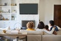 Back view of young family sitting on the sofa and watching TV together in their living room