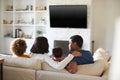 Back view of young family sitting on the sofa and watching TV together in their living room, close up Royalty Free Stock Photo