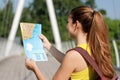 Back view of young female backpacker looking at a map on bridge in the forest. Girl reading a map for her journey in nature early