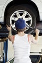 Back view of young female mechanic working on lifted car's tire in automobile repair shop Royalty Free Stock Photo