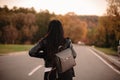 Back view of young female traveler wearing leather jacket and backpack walking on the road looking away Royalty Free Stock Photo