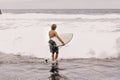 Back view of young fit surfer man with surfboard runs into ocean or sea with big waves for surfing. Concept of extreme Royalty Free Stock Photo