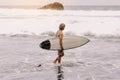 Back view of young fit surfer man with surfboard runs into ocean or sea with big waves for surfing. Concept of extreme Royalty Free Stock Photo