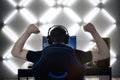 Back view of young gamer guy in headphones screaming and rejoicing unleash power while playing video games
