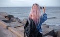 Back view of young girl with pink hair, wearing denim jacket and black backpack with steel thermo water bottle, taking photo. Royalty Free Stock Photo