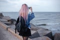 Back view of young girl with pink hair, wearing denim jacket and black backpack with steel thermo water bottle, taking photo. Royalty Free Stock Photo