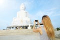 Back view of young girl taking photo by smartphone Buddha statue in Phuket, Thailand.