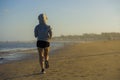 Back view of young happy and attractive fit woman in hoddie running on the beach in outdoors jogging workout in fitness training a Royalty Free Stock Photo