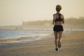 Back view of young happy and attractive fit woman running on the beach in outdoors jogging workout in fitness training and healthy Royalty Free Stock Photo