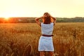 A back view of a young happy woman in a white summer dress and standing on a yellow farmer`s meadow with ripe golden wheat, Royalty Free Stock Photo