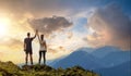 Back view of young hiker couple standing with raised arms holding hands on rocky mountain top enjoying sunset panorama Royalty Free Stock Photo