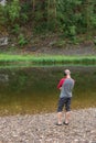 Back view of young hipster man listening to music in headphones on river bank. Far from big city bustle. Relaxing outdoors. Royalty Free Stock Photo