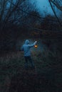 Back view of a young male with a lantern standing in front of a river on a spooky, scary evening