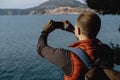 Back view of Young Male Traveler doing photo by phone on the background of the sea