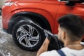 Young male worker washing the car wheels rims with a high pressure water gun after cleaning.