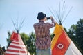 Back view of a young man tourist taking photo of teepee / tipi- native indian house with smartphone. Taking photo of wildlife.