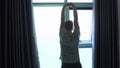 Back of view of young man unveil curtain and stretches arms in the morning. Slow motion