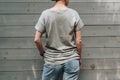 Back view. Young millennial woman dressed in gray t-shirt is stands against gray wood wall.