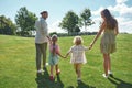 Back view of young parents holding hands together with their little kids, boy and girl and walking on green grass field Royalty Free Stock Photo