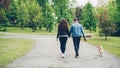 Back view of young people girlfriend and boyfriend walking the dog in city park in summer, man and woman are holding Royalty Free Stock Photo