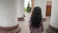 Back view of young pretty wonan walking along the columns