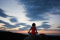 Back view of young slim woman sitting on big rock in yoga lotus pose on green tree tops evening sky Royalty Free Stock Photo