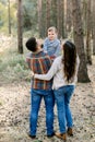 Back view of young stylish parents, father and mother, holding their little baby child boy, smiling at camera. Outdoor Royalty Free Stock Photo