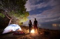 Young couple man and woman having rest at tourist tent and burning campfire on sea shore near forest Royalty Free Stock Photo