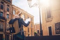 Back view. Young tourist woman in hat and with backpack is standing on city street and is looking for a way on map. Royalty Free Stock Photo