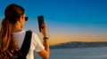 Back view of young tourist woman in packpack using smartphone take picture at Sunset scene of Caldera View ,Santorini,Greece Royalty Free Stock Photo