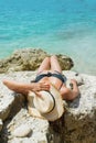 Back view young woman in black swimsuit and straw hat on wild snone beach with clean sea Royalty Free Stock Photo