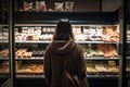 Back view of young woman in brown coat looking at different types of pastry in a bakery shop, A woman full rear view shopping in a