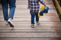 Back view on young woman and child in plaid shirt and blue jeans with a toy car running on wooden surface in the park