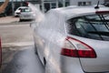 Back view of young woman cleaning her car on self service car. Female washing with jet sprayer. White foam on car Royalty Free Stock Photo