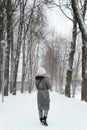 Back view of young woman in coat and knitted white hat enjoying walk in winter park, outdoors. Royalty Free Stock Photo