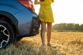 Back view of young woman driver slim legs in short yellow summer dress standing near her car on dry straw field Royalty Free Stock Photo