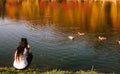 Back view of young woman feeding ducks while sitting by the lake during sunny weather Royalty Free Stock Photo