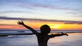 Back view of young woman feeling happy and freedom as silhouette with raised arms against calm sunset beach background Royalty Free Stock Photo