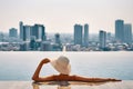 Back view of young woman in hat relaxing in swimming pool on the roof top of hotel and enjoy cityscape Royalty Free Stock Photo