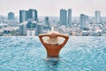 Back view of young woman in hat relaxing in swimming pool on the roof top of hotel and enjoy cityscape Royalty Free Stock Photo