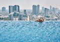 Back view of young woman in hat relaxing in swimming pool on the roof top of hotel and enjoy cityscape Royalty Free Stock Photo