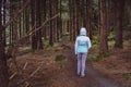 Back view of a young woman hiking in Irish forest. Hiking girl is walking in gloomy mystical and dark forest - thriller scene. Royalty Free Stock Photo