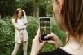 Back view of Young woman holding cell phone and making photo of her girl friend. Two girlfriends take pictures of each Royalty Free Stock Photo