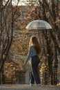 Back view on young woman with long hair walks through autumn park. Pretty girl with transparent umbrella