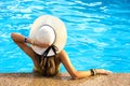 Back view of young woman with long hair wearing yellow straw hat relaxing in warm summer swimming pool with blue water on a sunny Royalty Free Stock Photo