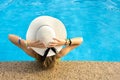 Back view of young woman with long hair wearing yellow straw hat relaxing in warm summer swimming pool with blue water on a sunny Royalty Free Stock Photo