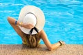 Back view of young woman with long hair wearing yellow straw hat relaxing in warm summer swimming pool with blue water on a sunny Royalty Free Stock Photo