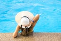 Back view of young woman with long hair wearing yellow straw hat relaxing in warm summer swimming pool with blue water on a sunny Royalty Free Stock Photo