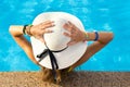 Back view of young woman with long hair wearing yellow straw hat relaxing in warm summer swimming pool with blue water on a sunny Royalty Free Stock Photo